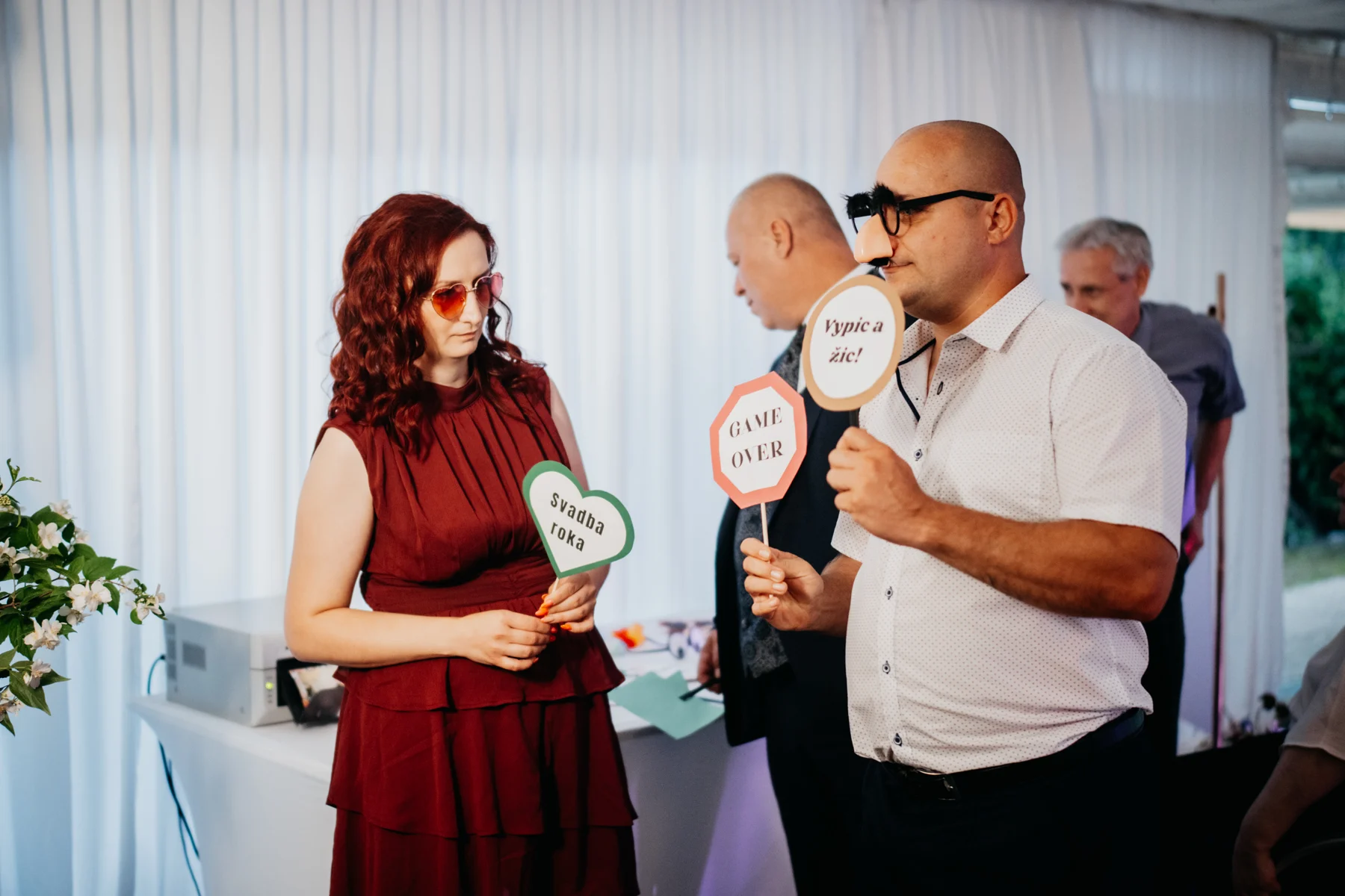 Svadobní hostia sa zabávajú s okuliarmi a tabuľkami pri fotoboxe